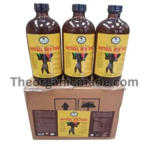 A photograph showing three large amber glass bottles of 'Natural Men Tonic, Extra Strong,' positioned side-by-side on top of a single, closed cardboard shipping box. Each bottle features a detailed yellow and black label with the brand logo and the product name. The shipping box has a larger version of the bottle label affixed to its front panel, displaying ingredient and nutritional information. The scene is illuminated in a clean, professional studio style, with all elements sharp and centered. A watermark with the text 'Theorganicmade.com' overlays the image.