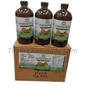 A high-angle photograph showing three amber glass bottles of 'Organic Parasite Formula' standing side-by-side on top of a single brown cardboard shipping box. The bottles and the box feature white and green labels that display the product name, key ingredient Wormwood (Artemisia absinthium), and images of a pumpkin and a broken papaya. Text on the labels reads 'BEST HELP WITH PARASITE CLEANSE' and 'RELIEF - SUPPORT - COMFORT'. The shipping box is also marked 'PGP GLASS' and has a transparent watermark 'Theorganicmade.com' overlaying the entire composition. The scene is set against a plain, off-white background.