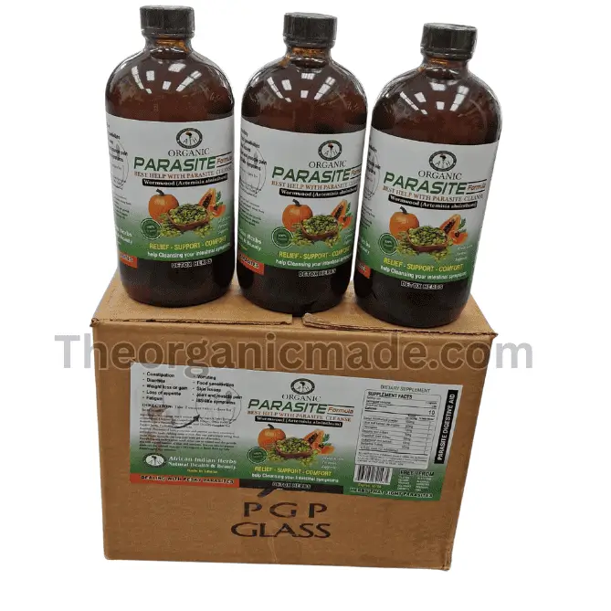 Parasite Cleanse Formula 16oz (Wholesale) 1 A high-angle photograph showing three amber glass bottles of 'Organic Parasite Formula' standing side-by-side on top of a single brown cardboard shipping box. The bottles and the box feature white and green labels that display the product name, key ingredient Wormwood (Artemisia absinthium), and images of a pumpkin and a broken papaya. Text on the labels reads 'BEST HELP WITH PARASITE CLEANSE' and 'RELIEF - SUPPORT - COMFORT'. The shipping box is also marked 'PGP GLASS' and has a transparent watermark 'Theorganicmade.com' overlaying the entire composition. The scene is set against a plain, off-white background.